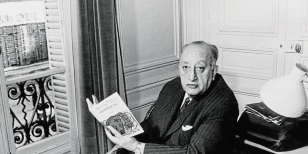 Miguel Ángel Asturias sentado junto a una ventana, sosteniendo un libro abierto.