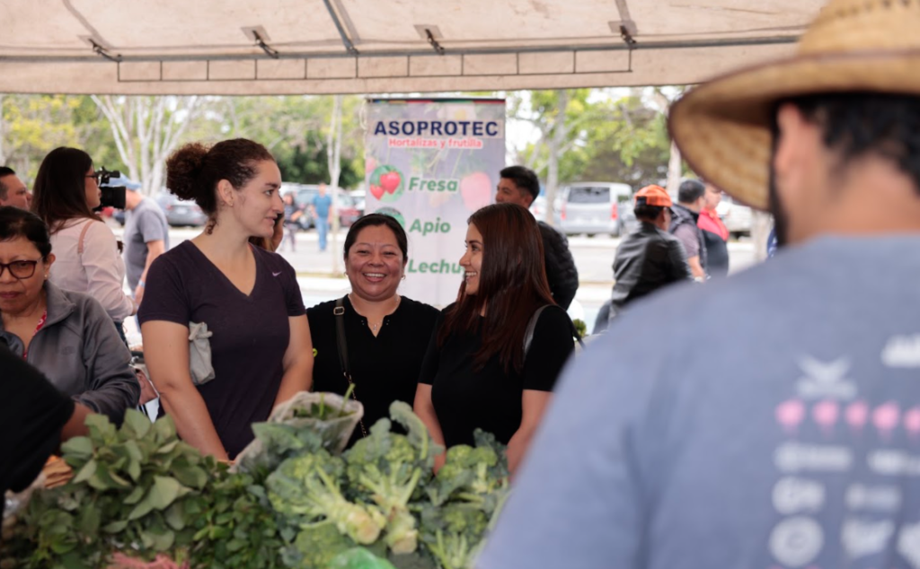 Productores y visitantes en un puesto de verduras de la Feria del Agricultor.